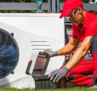Technicien en uniforme rouge installant une pompe à chaleur extérieure dans un jardin résidentiel