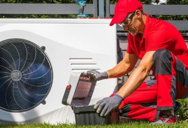 Technicien en uniforme rouge installant une pompe à chaleur extérieure dans un jardin résidentiel
