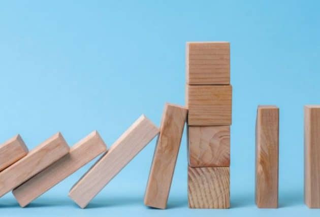 Effet domino stoppé par un mur de cubes en bois, symbolisant les 10 ans de protection contre les rattrapages excessifs de facturation d'énergie